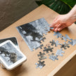Puzzle assembly of Bull vs Turtle Jigsaw Puzzle in Tin with detailed snowy mountain scene and tin box on a wooden table.