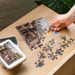 Pug, German Shepherd, Whippet, Basset Hound & Poodle Jigsaw Puzzle in Tin being assembled on a table with tin box nearby