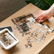 Person assembling German Shepherd Family Loft Jigsaw Puzzle in Tin with puzzle pieces and tin on wooden table.