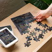 Gothic Angel Music Room Jigsaw Puzzle in Tin showing dark scene with angel in candlelit room, partially assembled on wooden table.