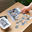 Assembling the Husky Family Winter Jigsaw Puzzle in Tin on a wooden table, showing pieces and the tin with image lid.