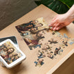 Hand assembling Modern Messiah Jigsaw Puzzle in Tin on wooden table, featuring symbolic modern and ancient elements.